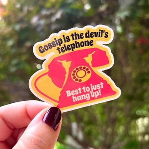 May include: A yellow and red sticker with a retro rotary phone design. The sticker says "Gossip is the devil's telephone. Best to just hang up!"