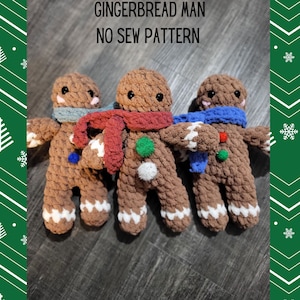 May include: Three brown crocheted gingerbread men with white detailing on their feet and arms. Each has a different coloured scarf: blue, red, and grey. The text "GINGERBREAD MAN NO SEW PATTERN" is at the top.