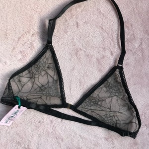 May include: Black lace bralette with a spiderweb pattern. The bralette has adjustable straps and a hook and eye closure at the back.