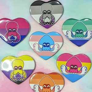 Könnte beinhalten: Sieben herzförmige Pins mit verschiedenen Farben von Pride-Flaggen und einem Cartoon-Tintenfisch-Design. Jeder Pin zeigt einen Tintenfisch in einer anderen Farbe mit einem Herz in einer anderen Farbe.