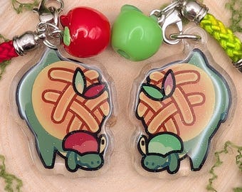 May include: Two acrylic charms featuring a green turtle with a lattice-crust pie shell, one with a red apple charm and red cord, the other with a green apple charm and lime green cord. Both charms have silver-toned metal lobster clasps.