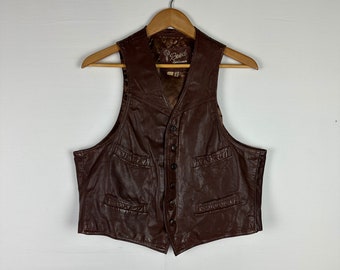 Puede incluir: Un chaleco de cuero marrón con cierre de botones y múltiples bolsillos. El chaleco tiene una etiqueta que dice "Reed Leatherwear".