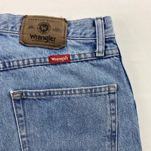 May include: Light blue denim jeans with a back pocket and a brown leather Wrangler label that says "Premium Quality" and "Authentic Jeans".