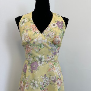 May include: A yellow halter dress with a floral print featuring purple, pink, and white flowers. The dress has a V-neckline and a fitted bodice.