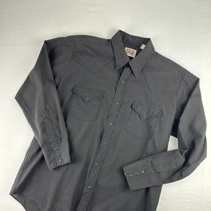May include: A black long-sleeved button-down shirt with a pointed collar and two chest pockets. The shirt has a brand label that reads "Ely Western Wear".