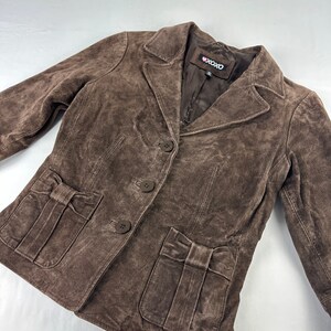 May include: A brown suede jacket with a button closure and two pockets with bow details. The jacket has a label that says "XOXO".