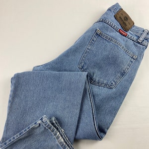 May include: Light blue denim jeans with a brown leather Wrangler label and a red Wrangler patch on the back pocket.