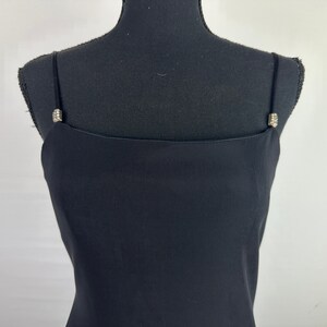 May include: A black sleeveless dress with a simple, straight neckline and a fitted bodice. The straps have small, sparkly embellishments.
