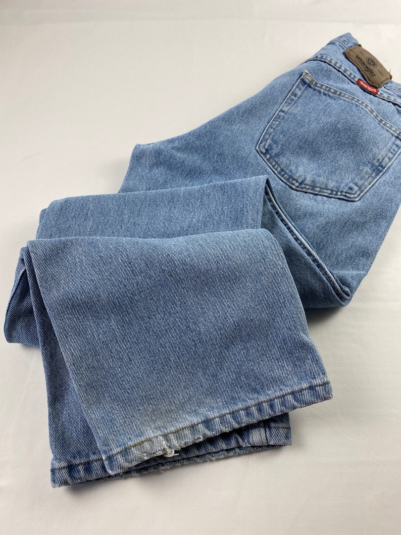 May include: A pair of light blue denim jeans with a Wrangler logo patch on the back pocket.