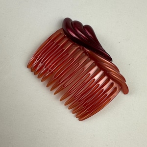 Puede incluir: Un peine para el cabello de plástico de color burdeos y naranja con un diseño decorativo de espiral.