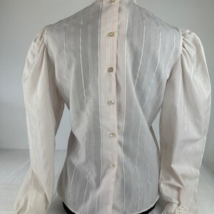 May include: White long-sleeve blouse with a high collar and lace trim. The blouse has a button-up back and a striped pattern.