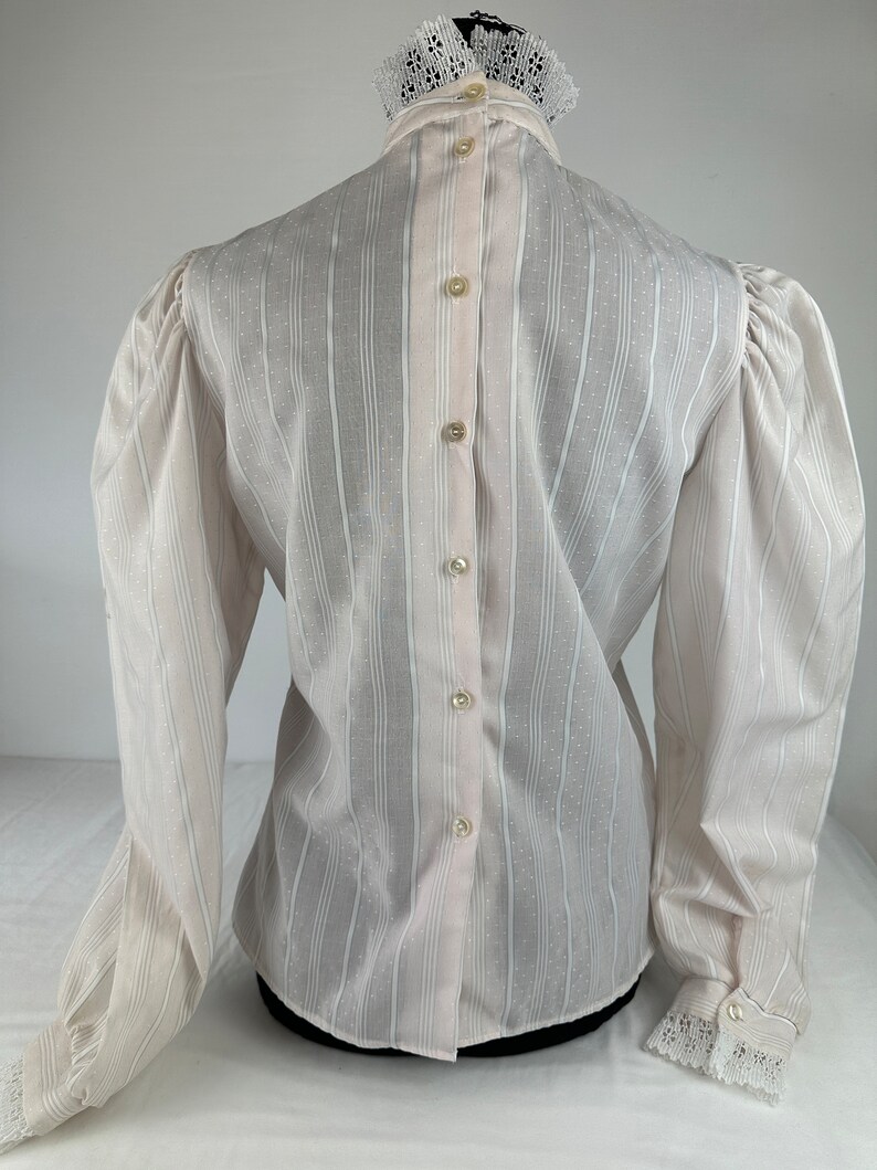 May include: White long-sleeve blouse with a high collar and lace trim. The blouse has a button-up back and a striped pattern.