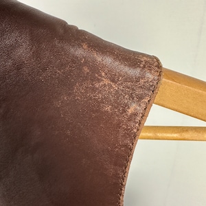 May include: Close-up of the brown leather shoulder of a jacket, showing the texture of the leather and the stitching along the edge.
