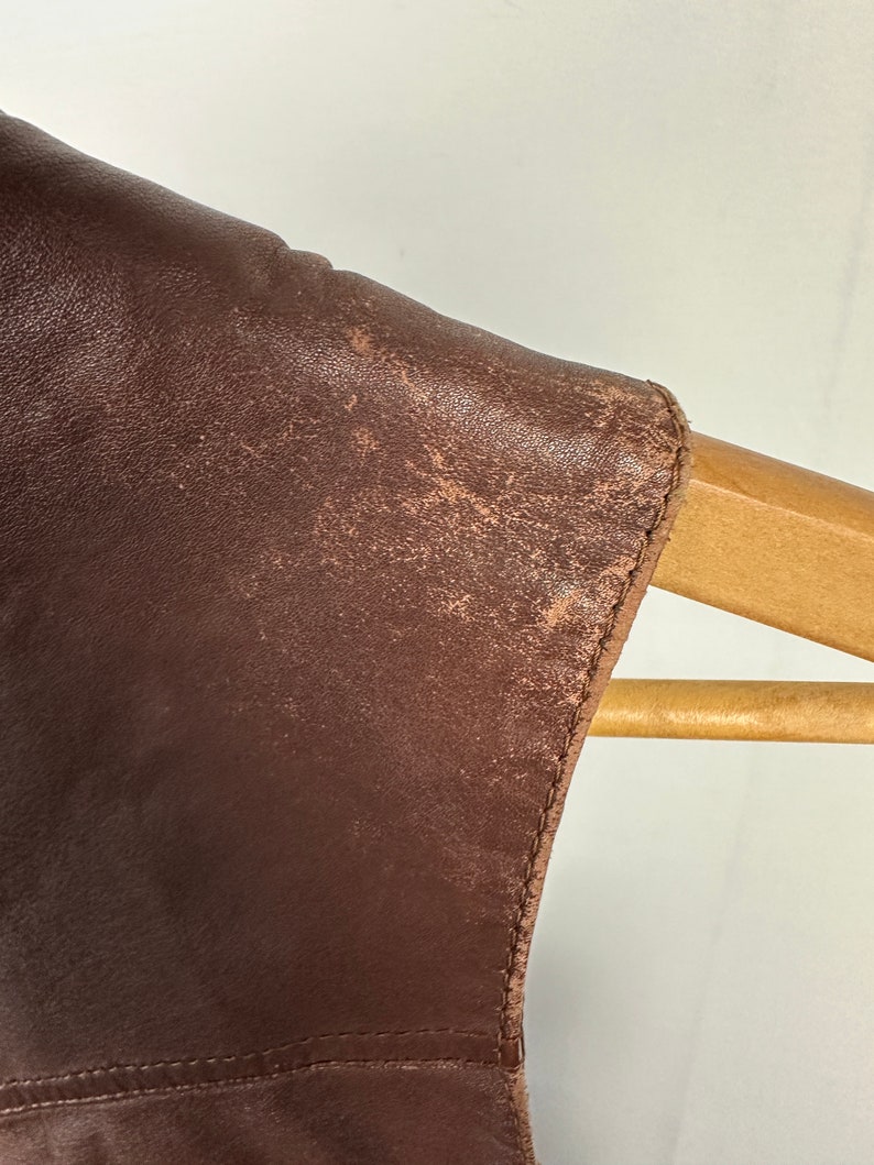 May include: Close-up of the brown leather shoulder of a jacket, showing the texture of the leather and the stitching along the edge.