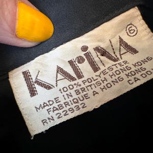 K&ouml;nnte beinhalten: Ein wei&szlig;es Etikett mit braunem Text, auf dem steht: "Karina&reg; 100% Polyester Hergestellt in Britisch-Hongkong Fabriqu&eacute; &agrave; Hong Kong RN 22932 CA 00118"