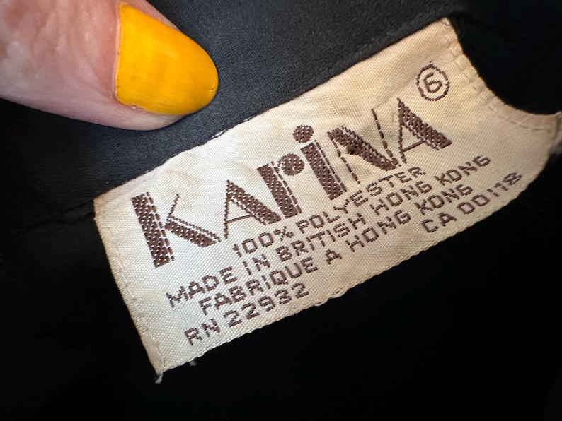 K&ouml;nnte beinhalten: Ein wei&szlig;es Etikett mit braunem Text, auf dem steht: "Karina&reg; 100% Polyester Hergestellt in Britisch-Hongkong Fabriqu&eacute; &agrave; Hong Kong RN 22932 CA 00118"
