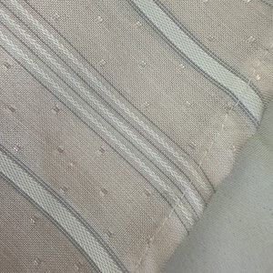 May include: Close-up of a beige fabric with thin white and gray stripes. The fabric has a subtle textured pattern.