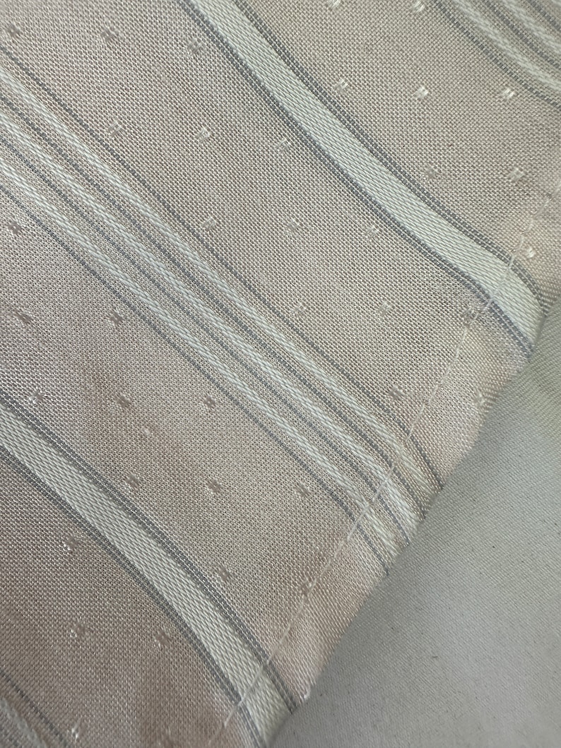 May include: Close-up of a beige fabric with thin white and gray stripes. The fabric has a subtle textured pattern.