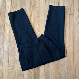 May include: Black pleated pants with a button closure. The pants are made of a smooth, wrinkle-resistant fabric.