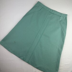 May include: A green and white gingham skirt with a straight cut and a button closure. The skirt has two pockets on the sides.