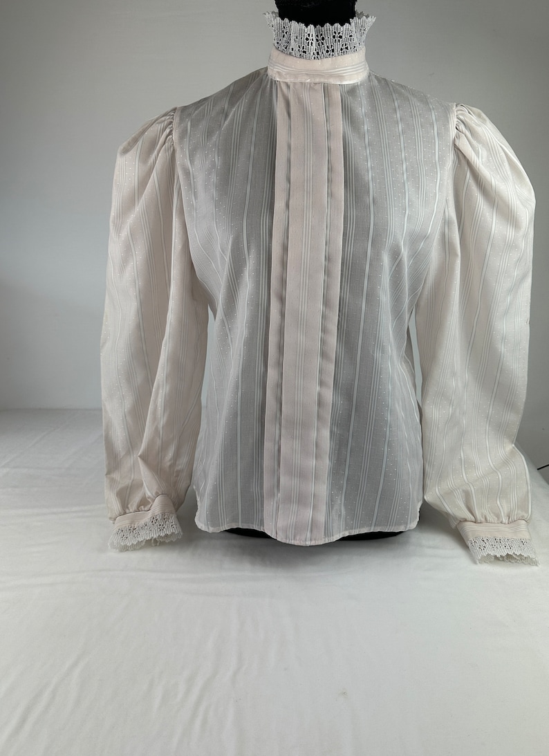 May include: A white sheer blouse with a high collar and long sleeves. The collar and cuffs have lace trim. The blouse has vertical stripes.
