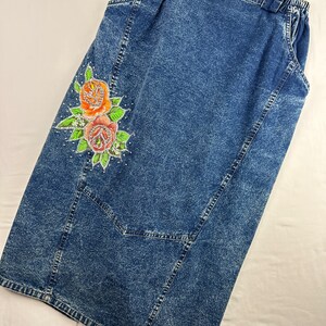 以下が含まれることがあります： 側面に花柄のデザインが施された青いデニムスカート。スカートは伸縮性のあるウエストバンドとポケットが付いています。