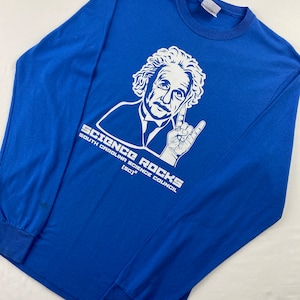 May include: A royal blue long-sleeve t-shirt with a white graphic of Albert Einstein giving a rock and roll hand gesture. The text "Science Rocks" is printed below the image, with the words "South Carolina Science Council (SCI)" printed below that.