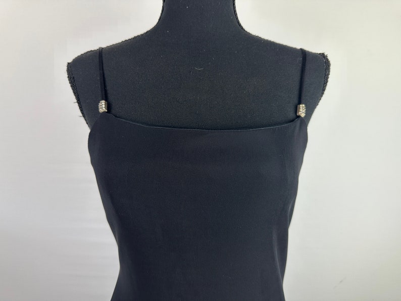 May include: A black sleeveless dress with a simple, straight neckline and a fitted bodice. The straps have small, sparkly embellishments.