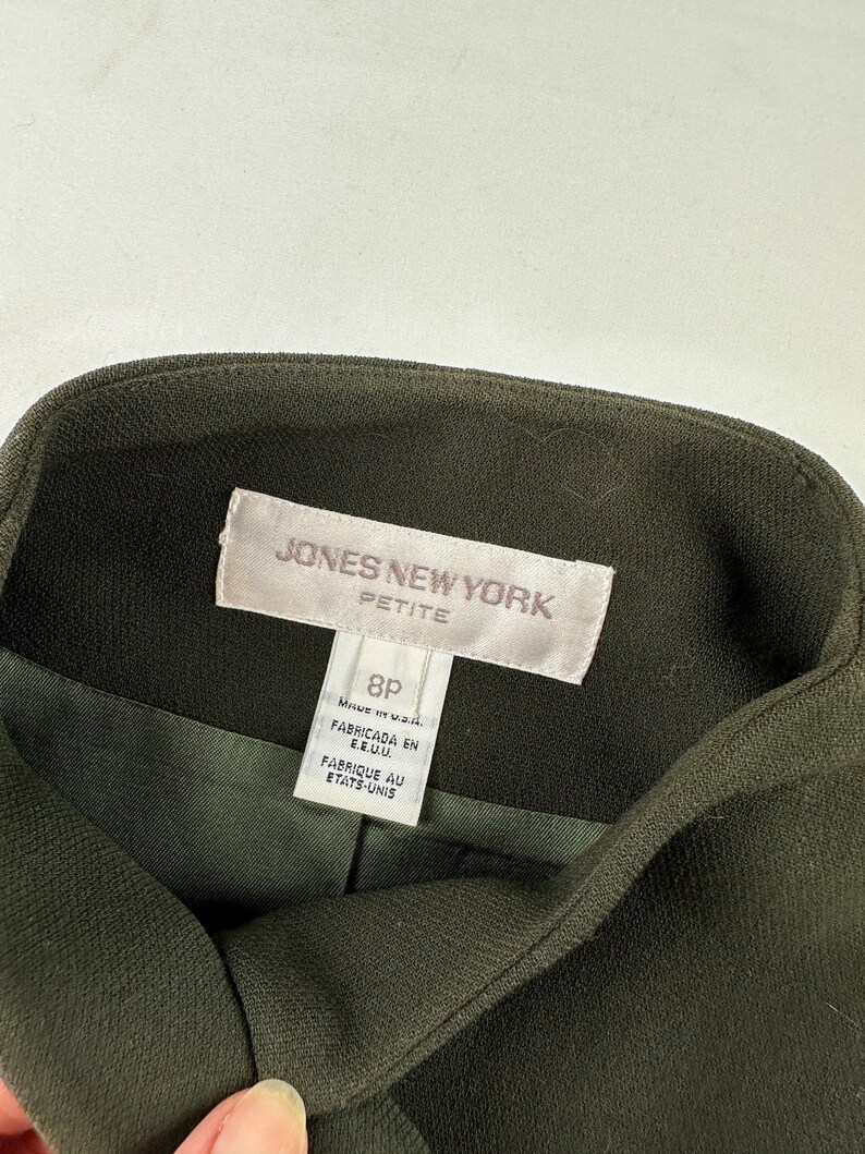 May include: A green blazer with a white label that reads "JONES NEW YORK PETITE" and "8P MADE IN U.S.A. FABRICADA EN E.E.U.U. FABRIQUE AU ETATS-UNIS".