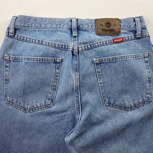 May include: A pair of light blue denim jeans with a brown leather patch that says "Wrangler" and a red tag that says "Wrangler" on the back.