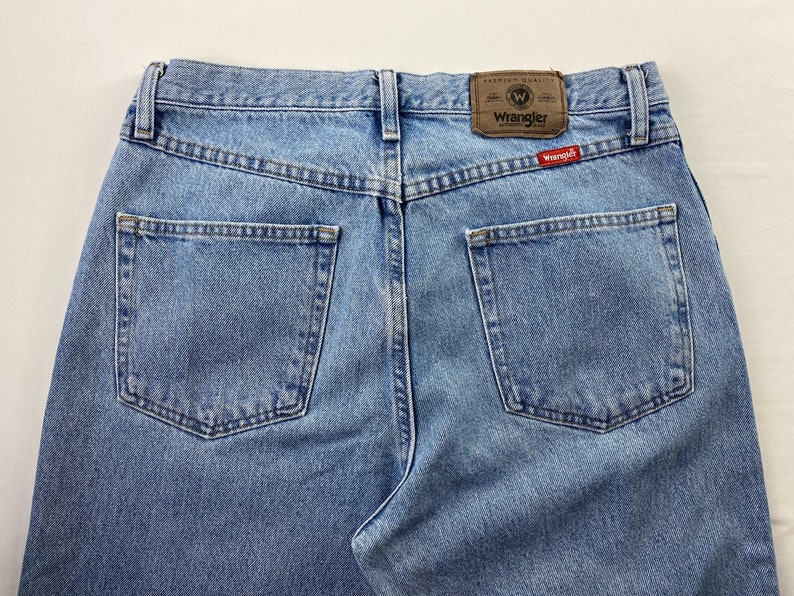 May include: A pair of light blue denim jeans with a brown leather patch that says "Wrangler" and a red tag that says "Wrangler" on the back.