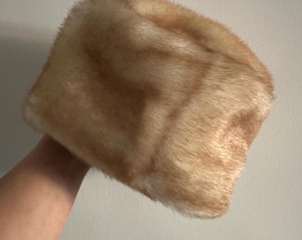 May include: A fluffy, light brown faux fur hat with a rounded shape.