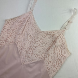 Op de afbeelding: Een lichtroze slip met delicate witte kantversiering rond de halslijn en armsgaten.