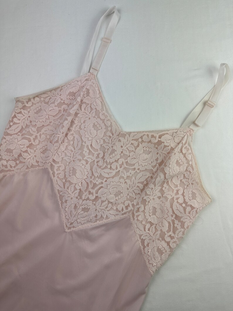 Op de afbeelding: Een lichtroze slip met delicate witte kantversiering rond de halslijn en armsgaten.