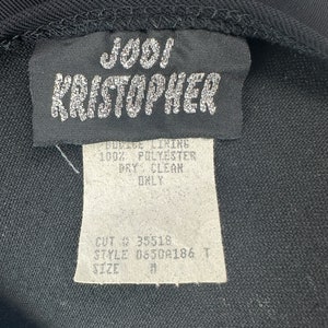 May include: Black clothing label with white text that reads "J001 KRISTOPHER", "PODICE LINING 100% POLYESTER DRY CLEAN ONLY", "CUT 35518", "STYLE 0650A186 T", and "SIZE".