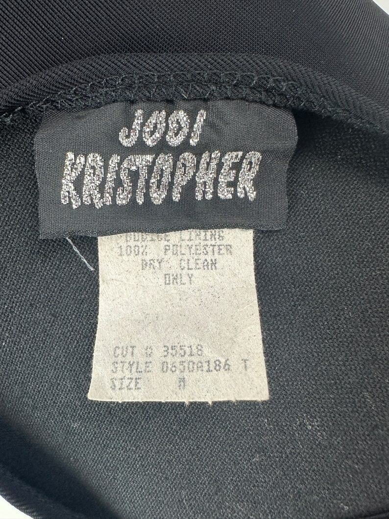 May include: Black clothing label with white text that reads "J001 KRISTOPHER", "PODICE LINING 100% POLYESTER DRY CLEAN ONLY", "CUT 35518", "STYLE 0650A186 T", and "SIZE".