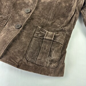 May include: A brown suede jacket with a bow detail on the front pocket and three buttons down the front.