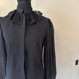 K&ouml;nnte beinhalten: Eine schwarze Bluse mit langen &Auml;rmeln und einem Spitzenkragen. Die Bluse hat einen Knopfleisten vorne und durchsichtige &Auml;rmel.