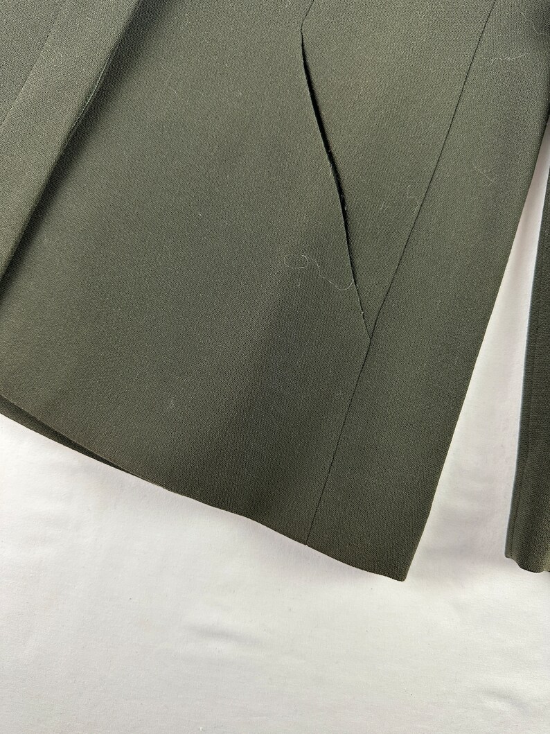 May include: A dark green blazer with a single pocket on the left side. The blazer is made of a smooth, textured fabric.