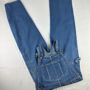 May include: A pair of blue denim overalls with adjustable straps and multiple pockets. The overalls are laid flat on a white surface.