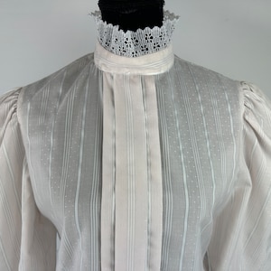 May include: White long-sleeved blouse with a high collar and a lace trim. The blouse has a vertical striped pattern and a sheer fabric.