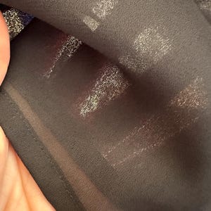 K&ouml;nnte beinhalten: Nahaufnahme eines schwarzen, durchsichtigen Stoffes mit einem dezenten Schimmer. Der Stoff hat eine strukturierte Oberfl&auml;che und ist &uuml;ber sich selbst gelegt.