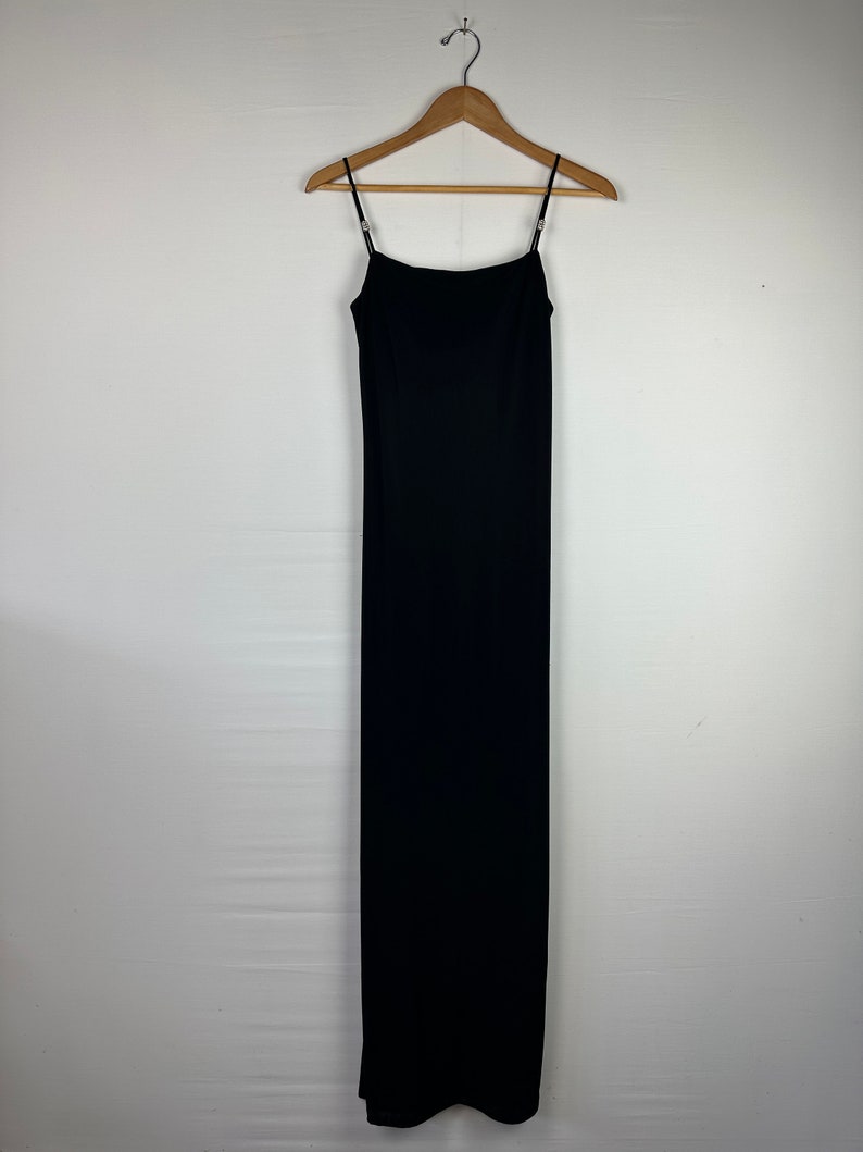 May include: A black maxi dress with thin straps hanging on a wooden hanger against a white background.