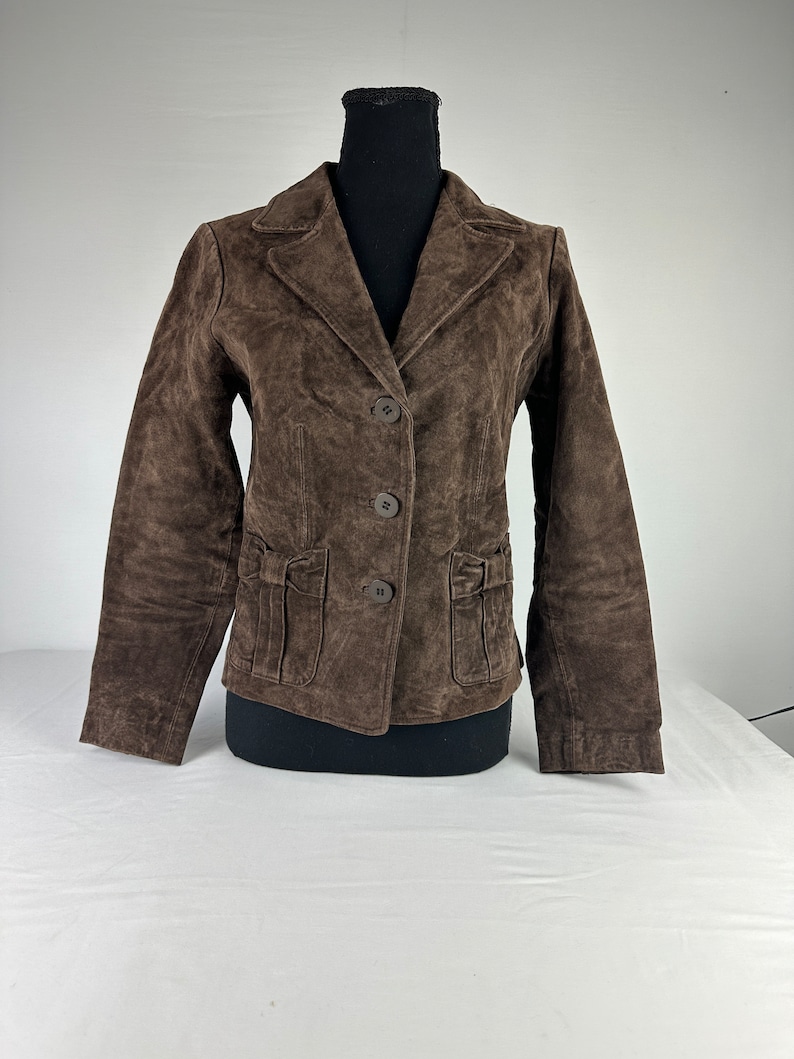 May include: A brown suede jacket with a button closure and pockets. The jacket has a classic style and is perfect for layering.