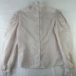 May include: A white striped long-sleeved blouse with a lace collar and cuffs. The blouse has a button-up front.