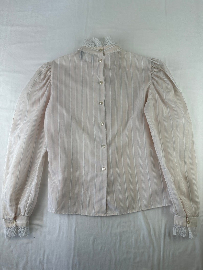 May include: A white striped long-sleeved blouse with a lace collar and cuffs. The blouse has a button-up front.