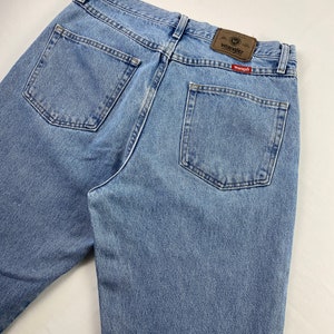 May include: A pair of light blue denim jeans with a brown leather Wrangler label on the back pocket. The label has the Wrangler logo and the text "Premium Quality".