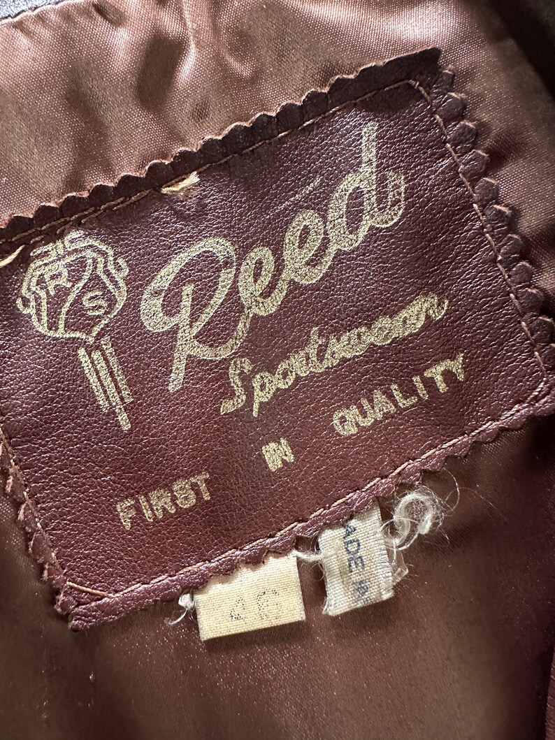 May include: A brown leather label with the text "Reed Sportswear First in Quality" in gold lettering. The label has a decorative scalloped edge.