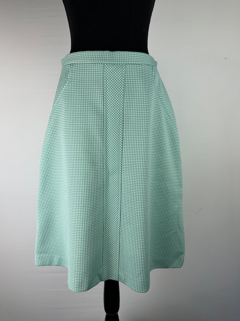 May include: A green and white gingham skirt with a straight, A-line silhouette. The skirt has a center seam and a simple, fitted waistband.