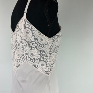 Op de afbeelding: Een witte slip van kant met een delicaat bloemenpatroon. De slip is gemaakt van een transparante stof en heeft verstelbare bandjes.